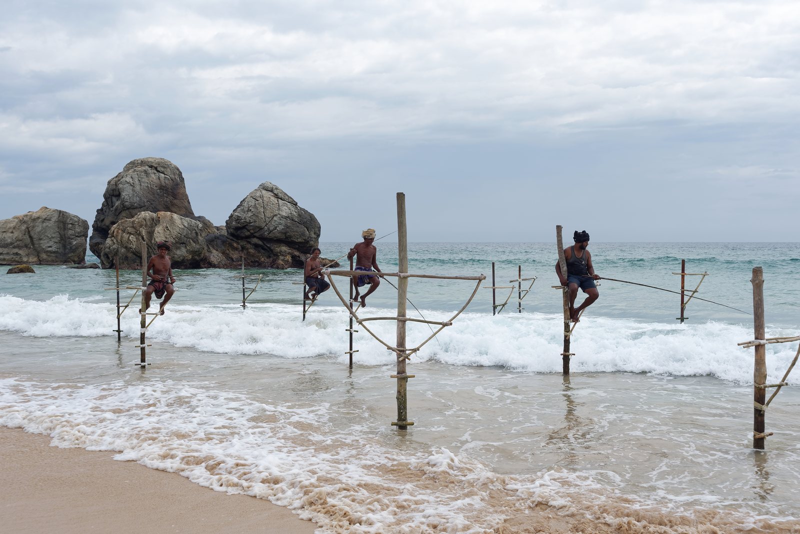 Stilt fishermen sitting on poles in the surf