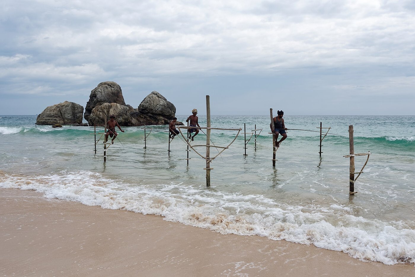 Stilt fishermen on poles in the surf